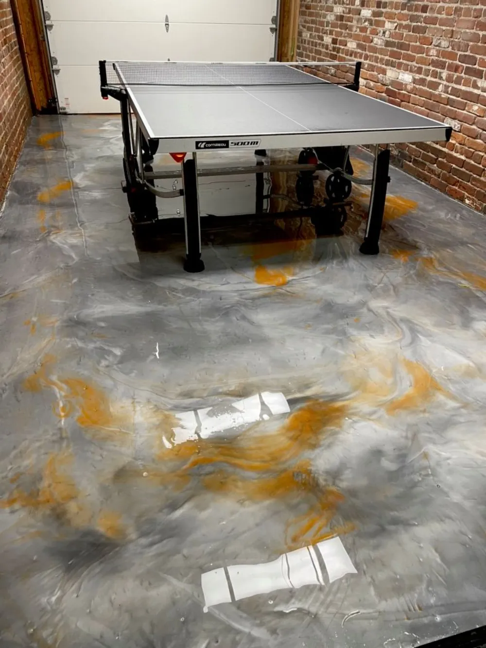 Gray and gold marbled metallic epoxy floor in a Denver game room with brick walls